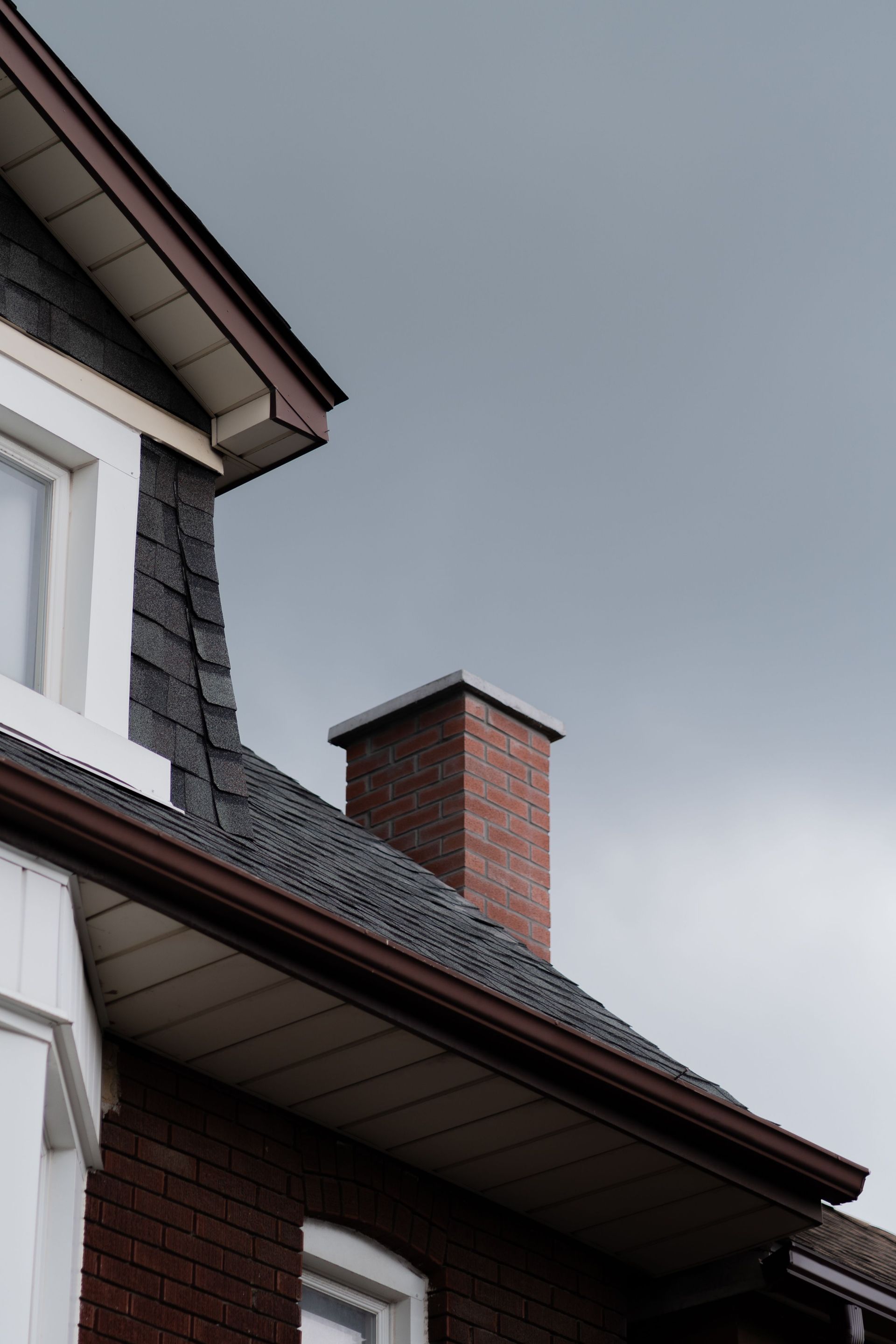 Close-up of a house roof with a brick chimney against a cloudy sky.